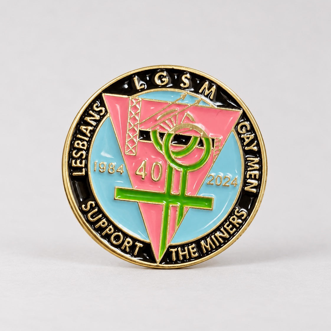 A round enamel pin with a gold-tone border and multicolor design, featuring the text 'LESBIANS G.S.